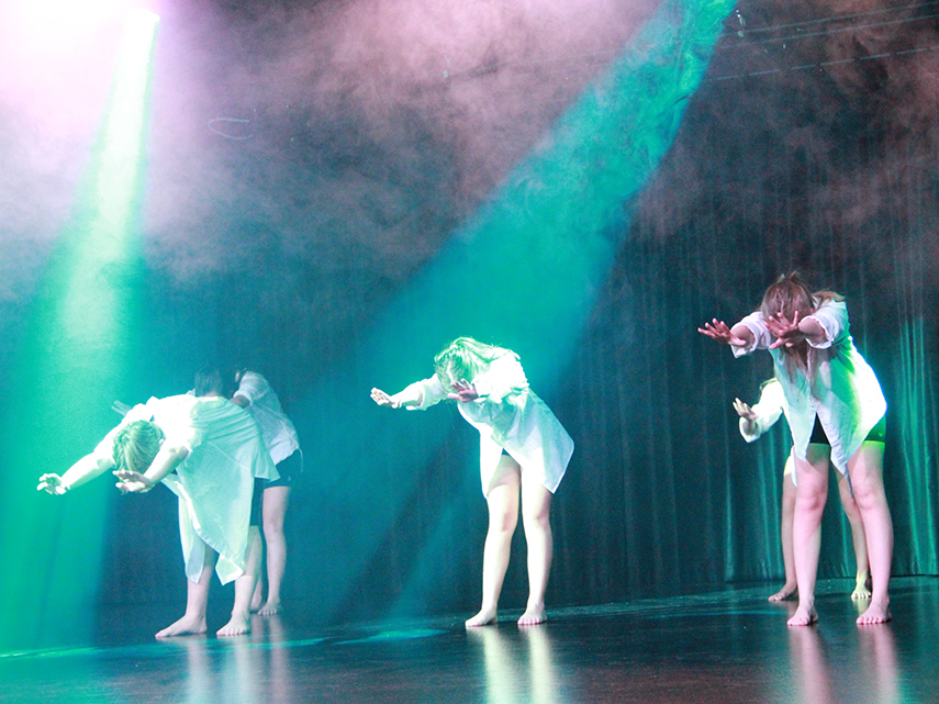 Några ungdomar i vita skjortor dansar i strålkastarljus på en scen