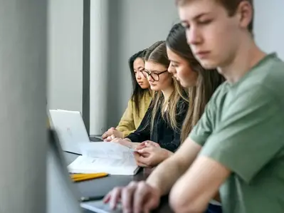Elever sitter vid sina datorer och studerar intensivt tillsammans.