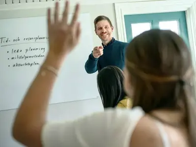 En lärare håller en lektion i projektledning medan en elev räcker upp handen för att ställa en fråga.